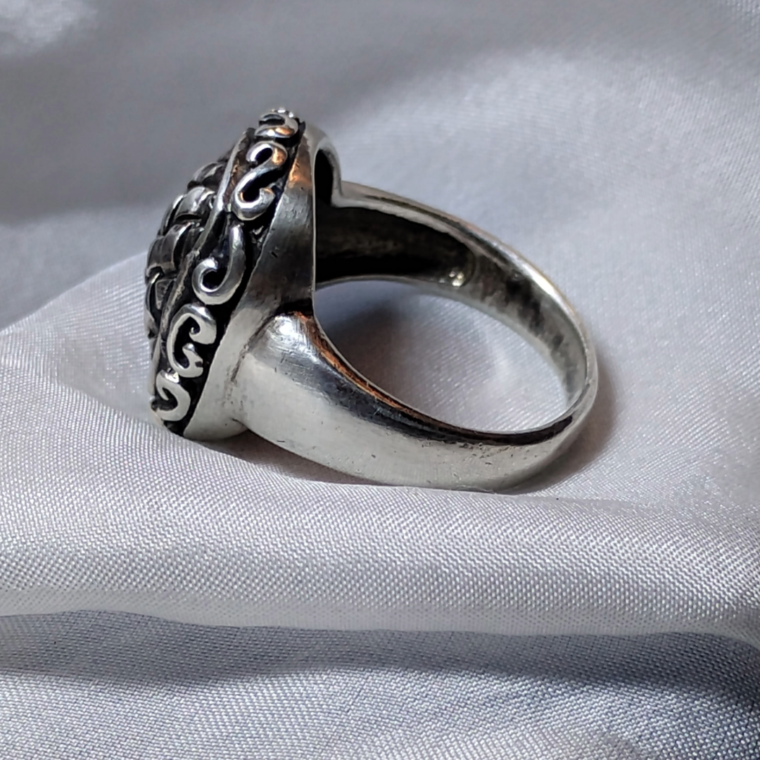 Silver ring with an ornate, raised basket-weave pattern centerpiece, framed by a decorative border.