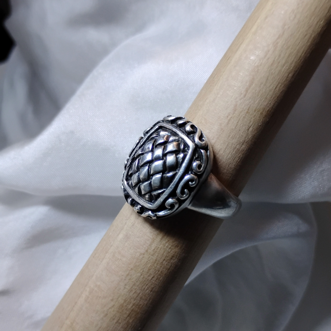 Silver ring with an ornate, raised basket-weave pattern centerpiece, framed by a decorative border.