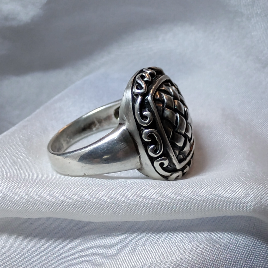 Silver ring with an ornate, raised basket-weave pattern centerpiece, framed by a decorative border.