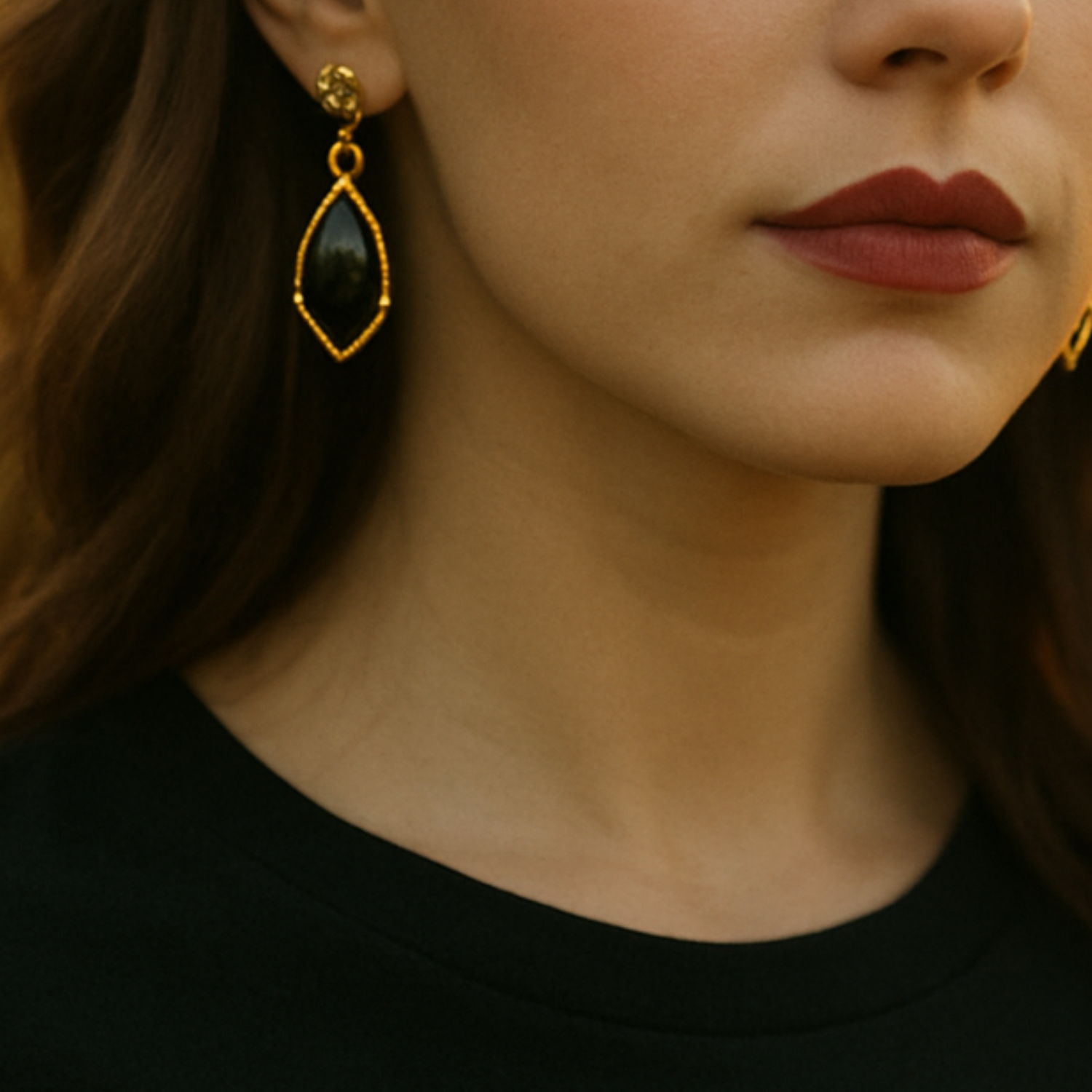 A woman in a field at sunset wearing a pair of gold and black onyx earrings from Violet Dreamer