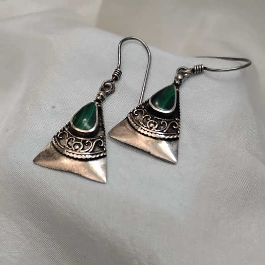 A pair of triangular sterling silver drop earrings with ornate filigree detailing and teardrop-shaped green malachite stones, displayed on a soft light gray fabric.