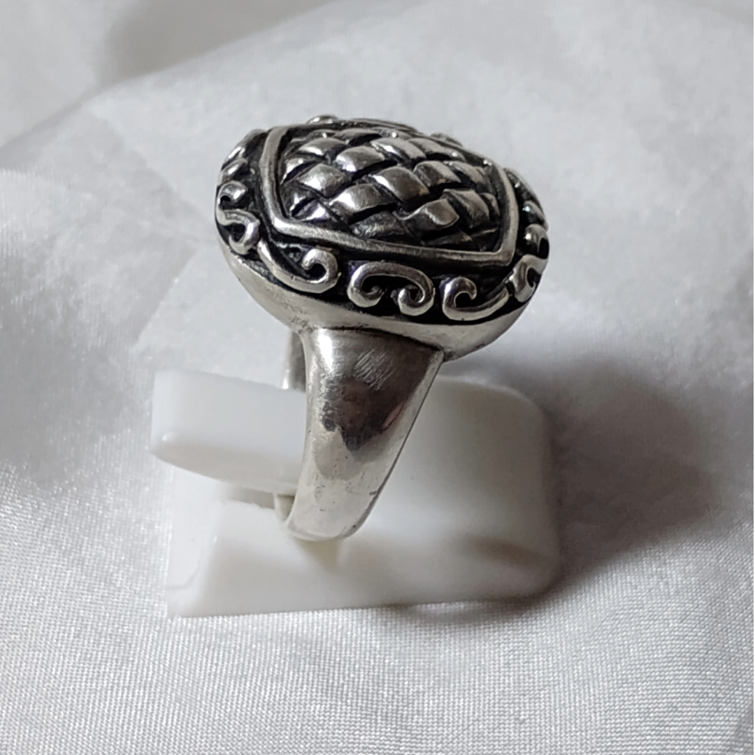 Silver ring with an ornate, raised basket-weave pattern centerpiece, framed by a decorative border.