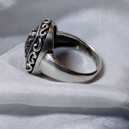 Silver ring with an ornate, raised basket-weave pattern centerpiece, framed by a decorative border.