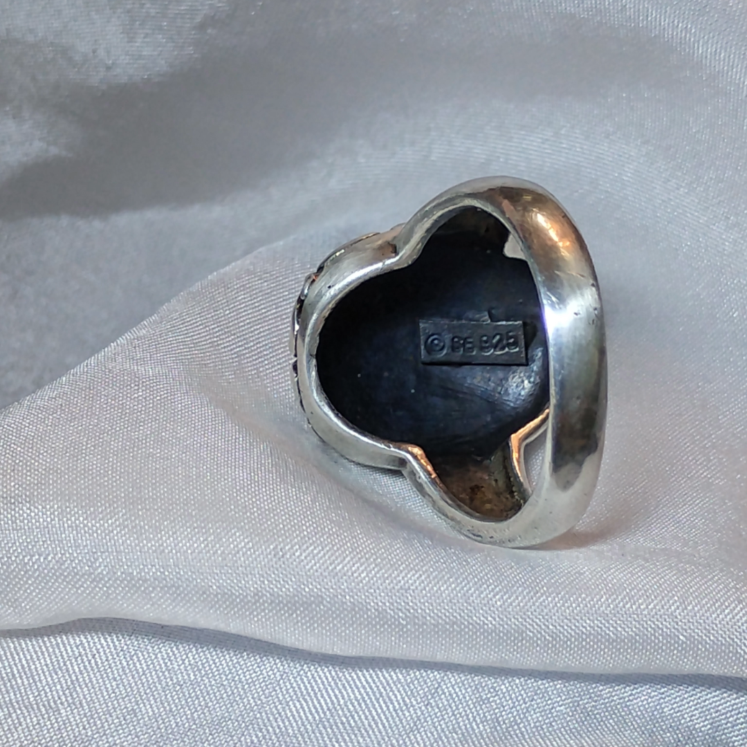 Silver ring with an ornate, raised basket-weave pattern centerpiece, framed by a decorative border.