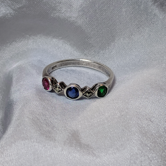 Vintage sterling silver ring featuring a trio of gemstones: a deep blue sapphire as the center stone, flanked by a vibrant red ruby and a rich green emerald, set in an elegant, timeless design.