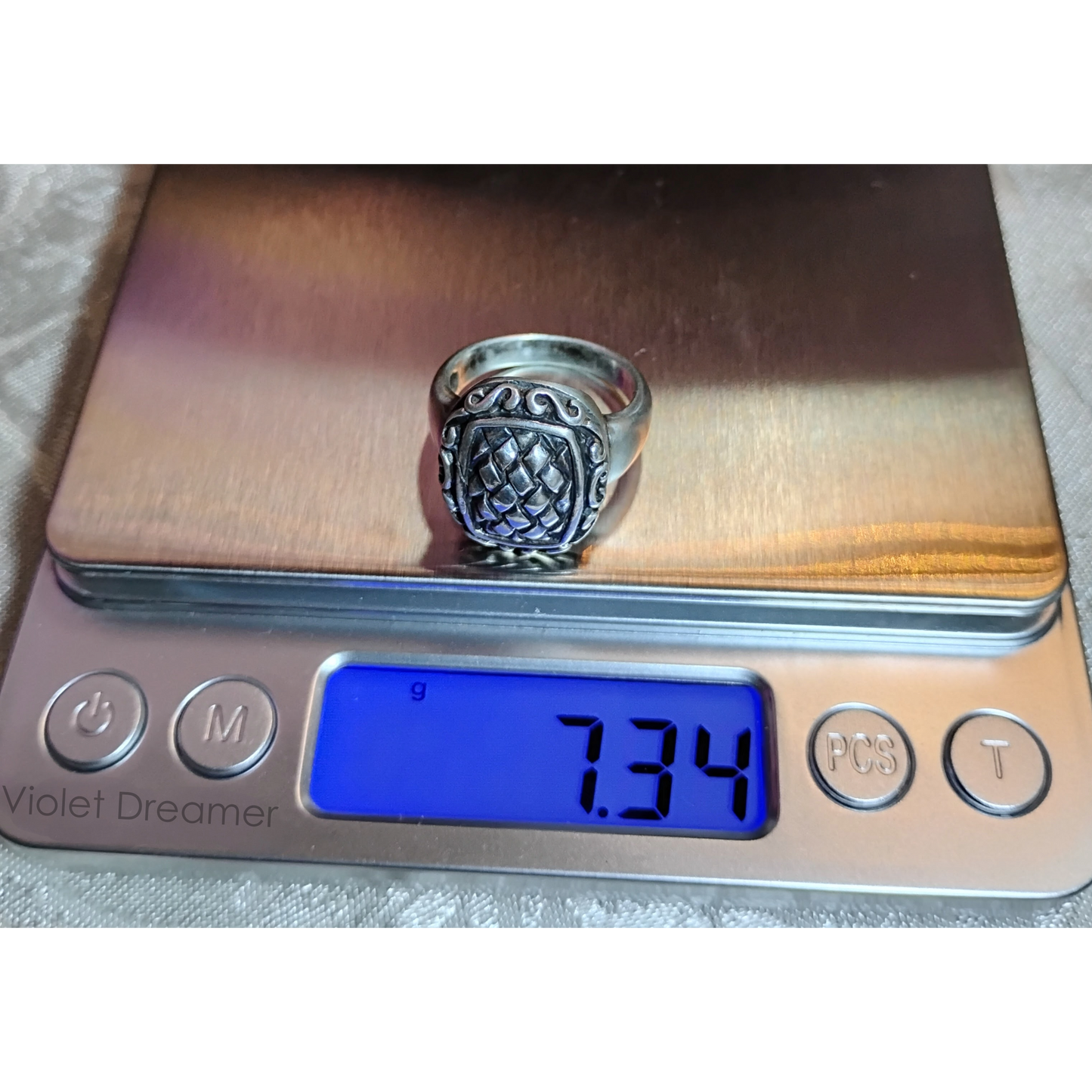 Silver ring with an ornate, raised basket-weave pattern centerpiece, framed by a decorative border.