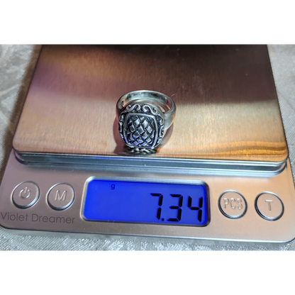 Silver ring with an ornate, raised basket-weave pattern centerpiece, framed by a decorative border.
